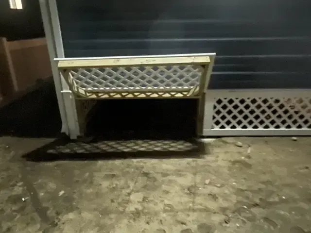 A white lattice fence with a shadow on the ground
