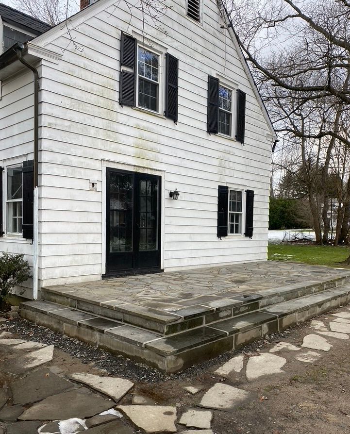 A white house with black shutters and a patio in front of it.