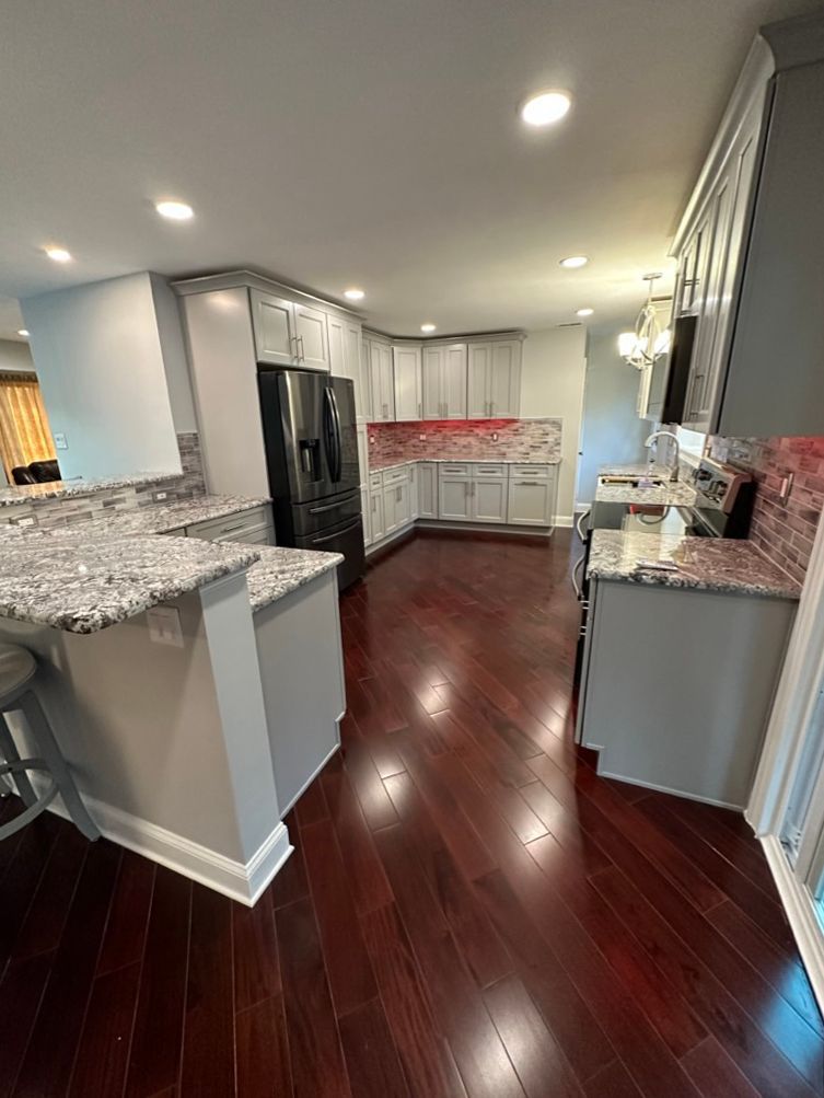 A kitchen with hardwood floors , granite counter tops , stainless steel appliances and white cabinets.