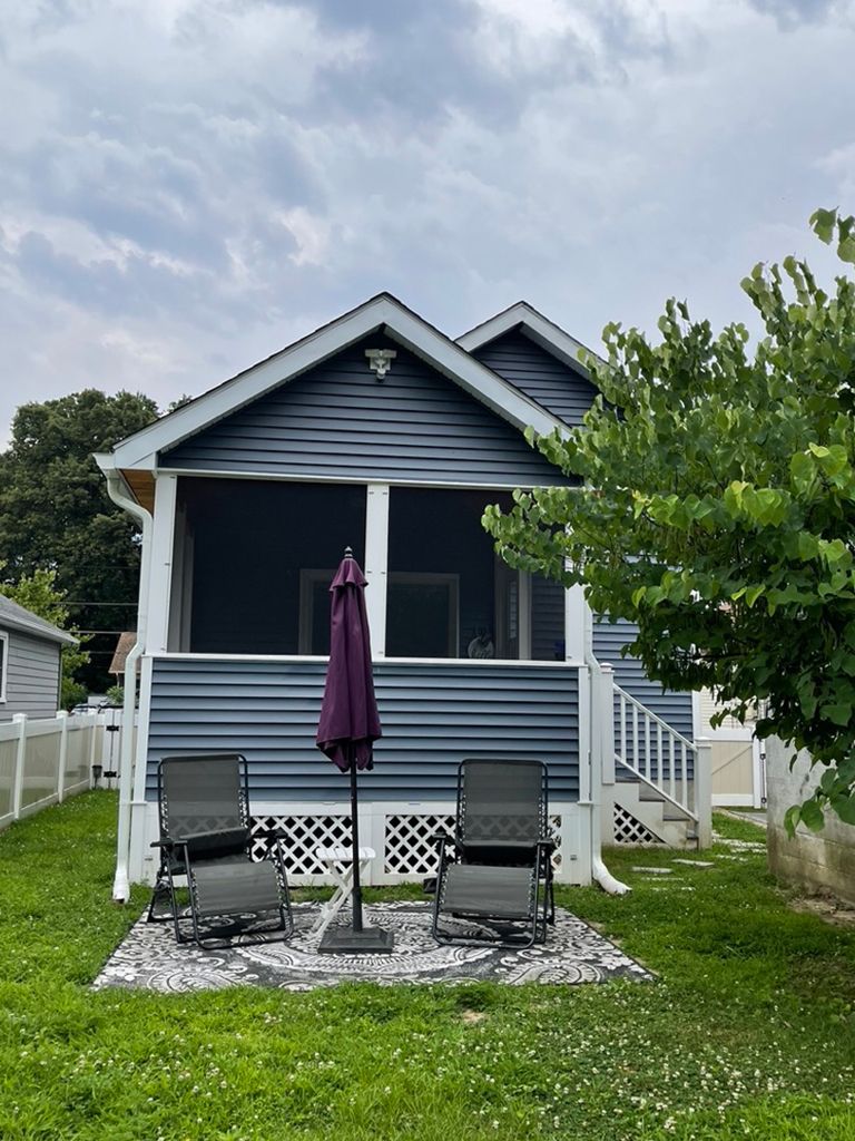 A blue house with a purple umbrella and chairs in front of it.