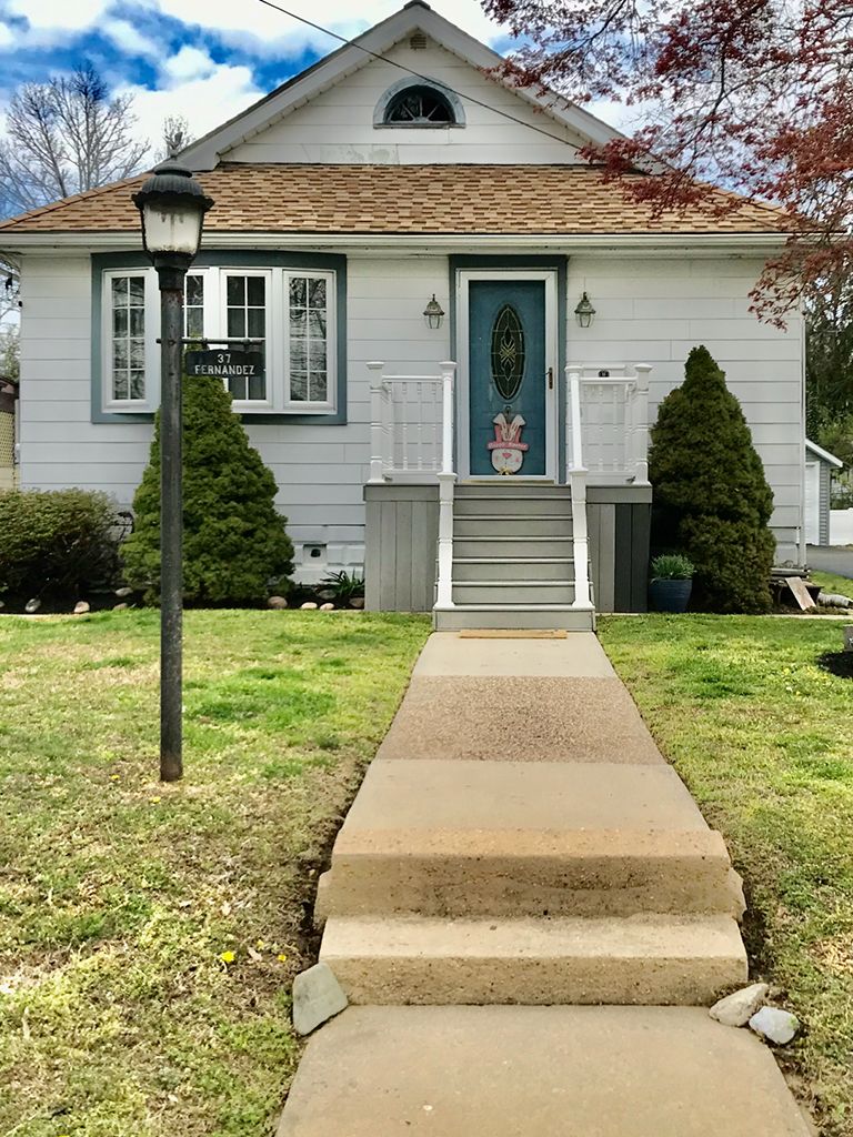 A white house with a blue door and a concrete walkway leading to it.