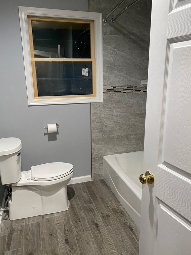 A bathroom with a toilet , tub and window.