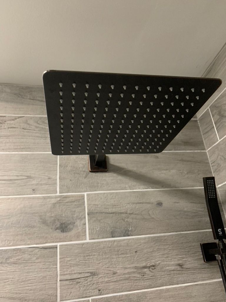 A black square shower head is hanging from the ceiling in a bathroom.