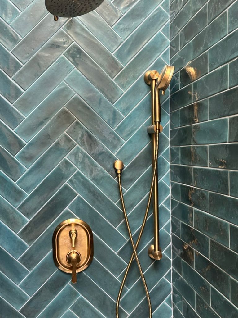 A shower with blue tiles and a gold shower head.