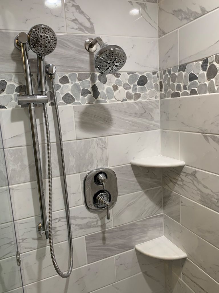 A shower with two shower heads and a corner shelf.