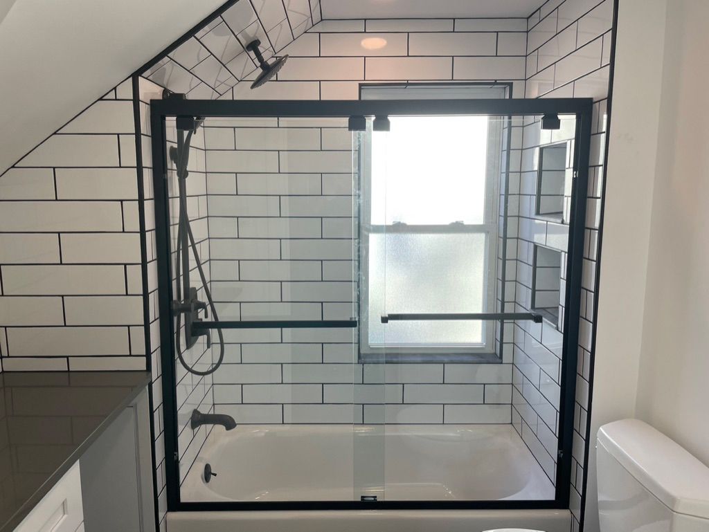 A bathroom with white tiles and a black shower door
