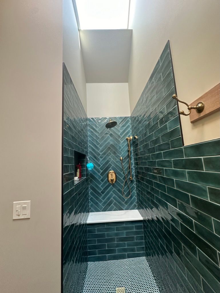 A bathroom with a walk in shower with green tiles and a skylight.