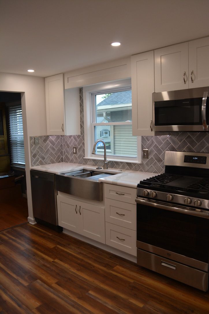 A kitchen with white cabinets , stainless steel appliances , a sink , stove and microwave.