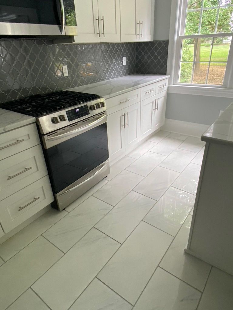 A kitchen with white cabinets , a stove , a microwave , and a window.
