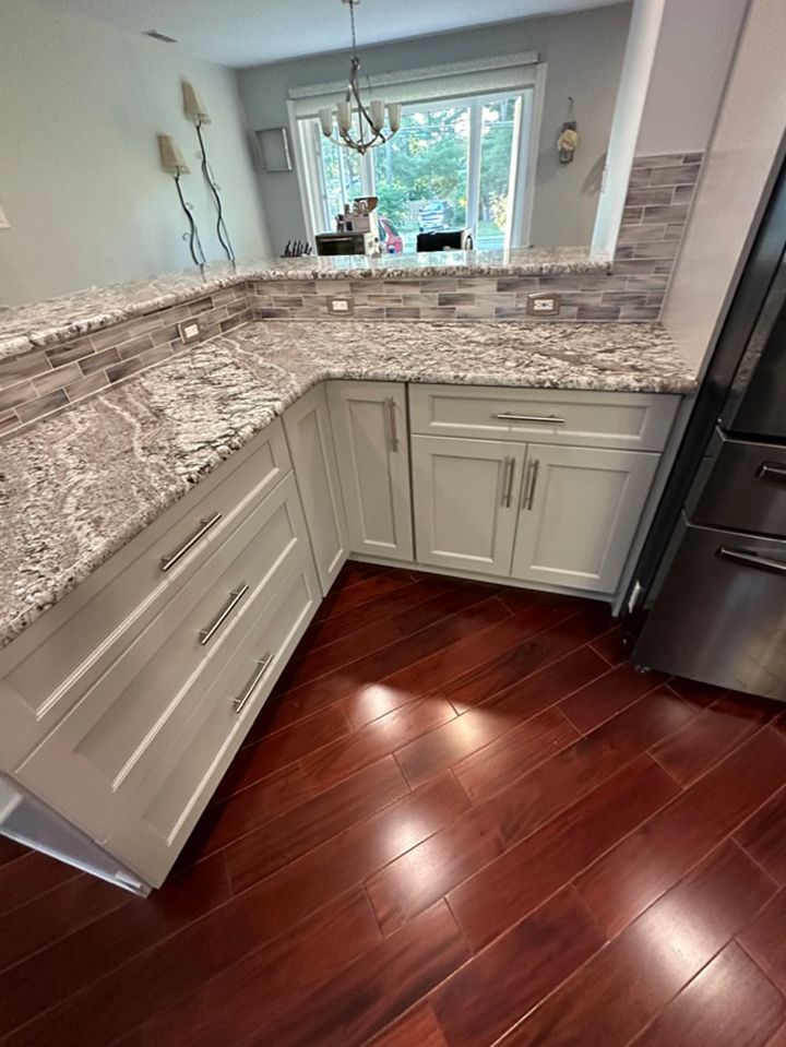 A kitchen with white cabinets , granite counter tops , and hardwood floors.