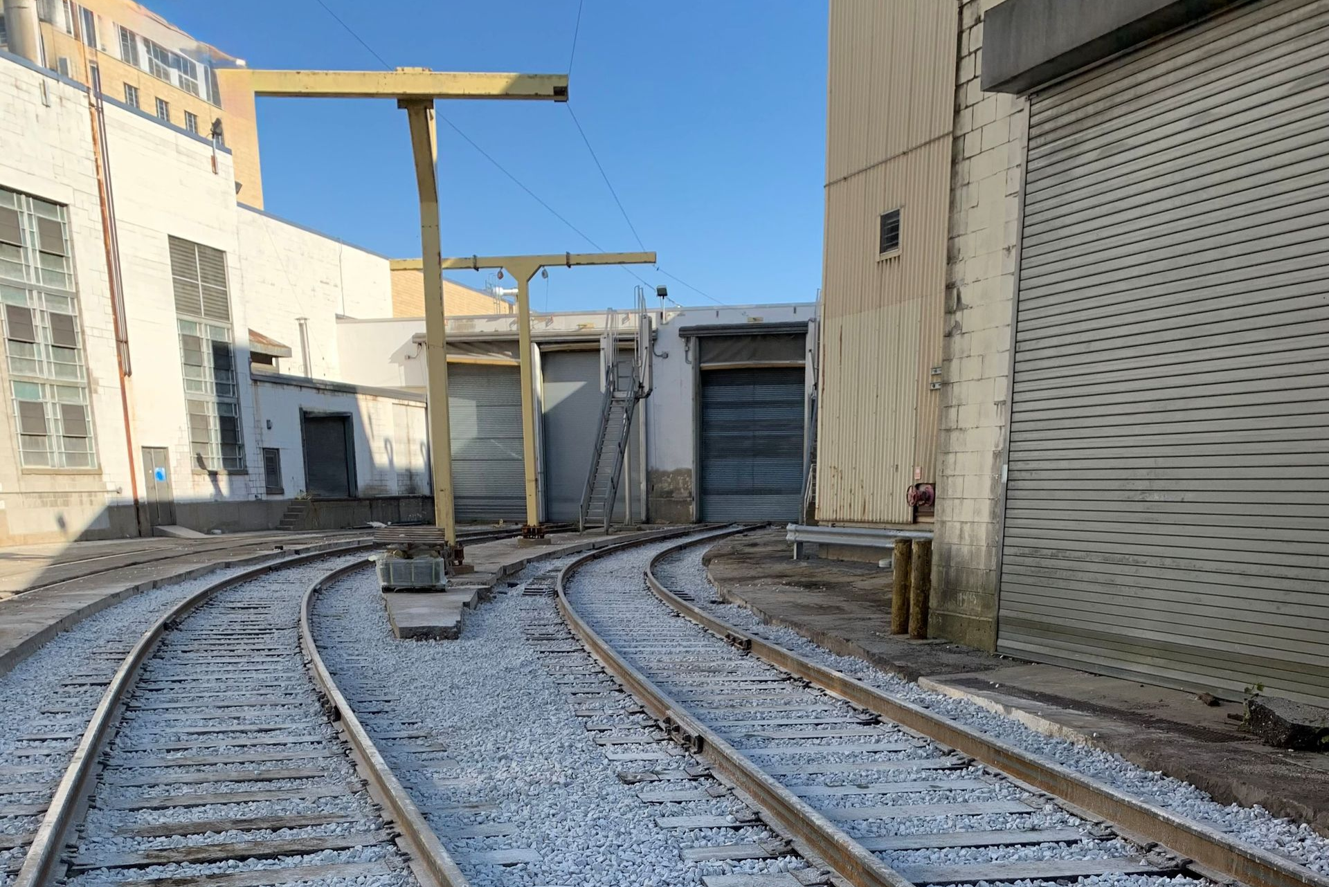 Railway tracks curving through a gravel bed, leading toward industrial buildings.
