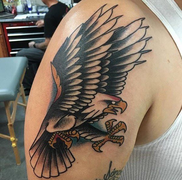 Bald eagle tattoo on shoulder, wings spread, black and gray with red and yellow accents.
