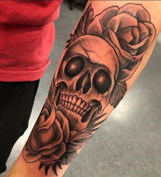 Tattoo of a skull with roses on forearm, black and gray shading.
