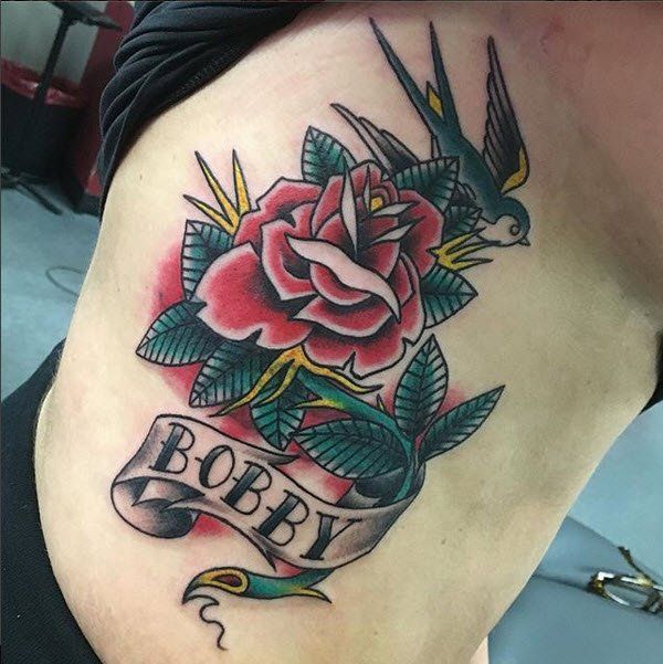 Tattoo on torso: red rose, green leaves, banner with
