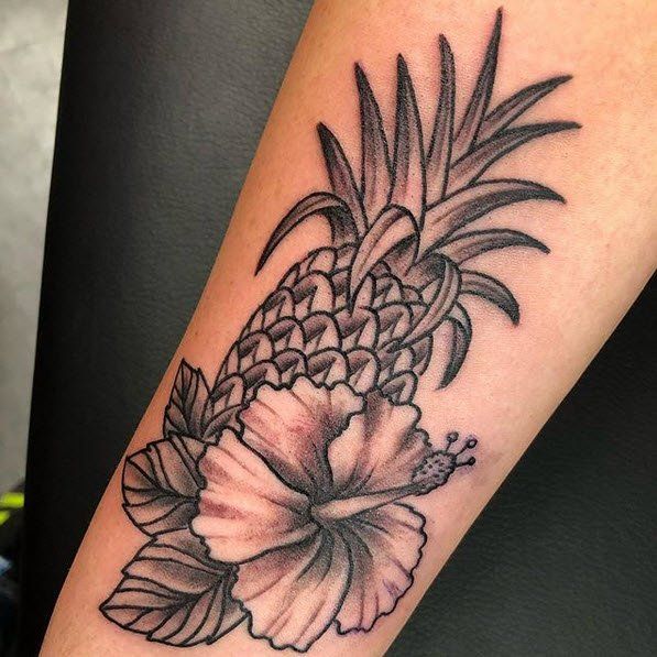 Black and white tattoo of pineapple and hibiscus flower on arm.