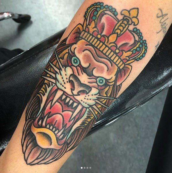 Lion head tattoo with crown; snarling expression, vibrant colors on arm.