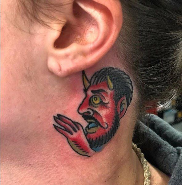 Tattoo of a red devil with a beard and horns on the neck, next to a person's ear.