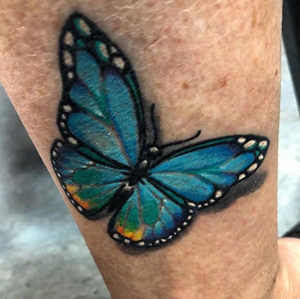 Blue butterfly tattoo on arm, with black outline and white details.