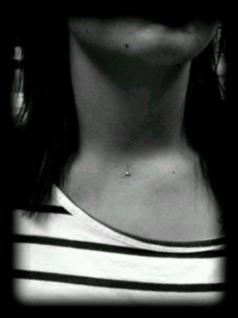 Black and white photo of a person's neck and upper chest. A piercing is visible on their collarbone, and they're wearing a striped shirt.