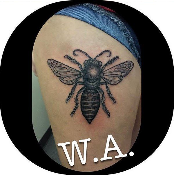 Tattoo of a black and gray bee on a person's arm, with the initials