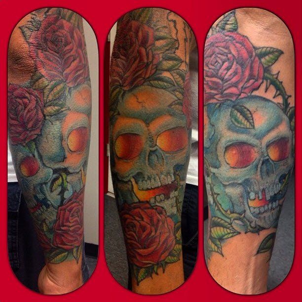 Tattoo of a skull with red roses, turquoise and red color scheme, on a person's arm.