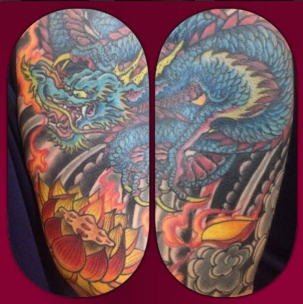 Blue dragon tattoo on an arm, with flames, lotus flowers, and dark clouds.