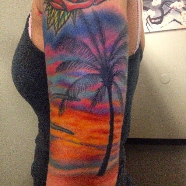 Palm tree silhouette tattoo on an arm with vibrant sunset colors of orange, pink, and blue.