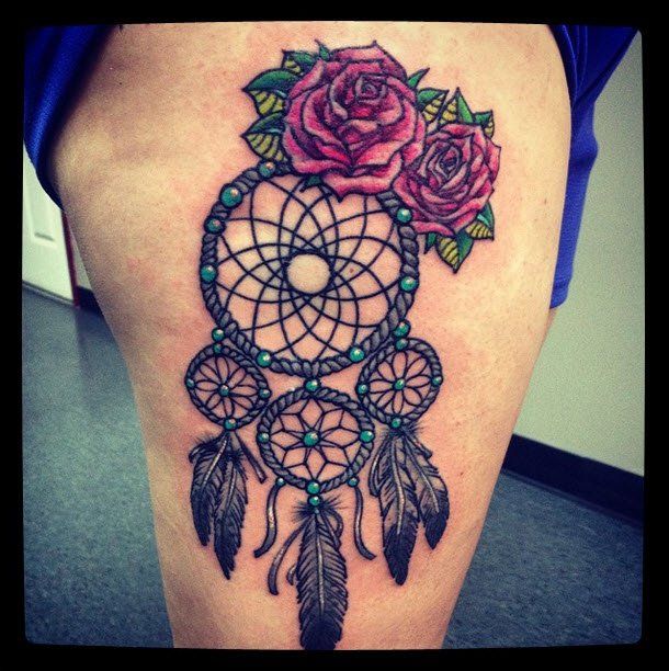 Tattoo of a dreamcatcher with two pink roses on a person's thigh.