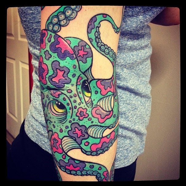 Colorful octopus tattoo on an arm, green with purple and pink spots, in front of a gray shirt.