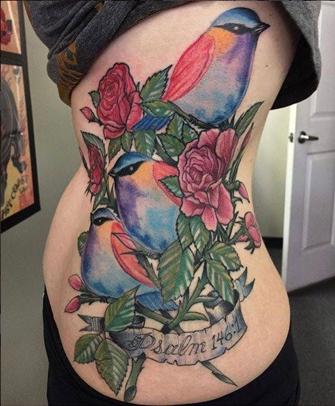 Tattoo of three colorful birds and roses on a person's side; a banner reads