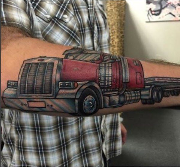 Tattoo of a red and gray semi-truck on a person's forearm, with a checkered shirt in the background.