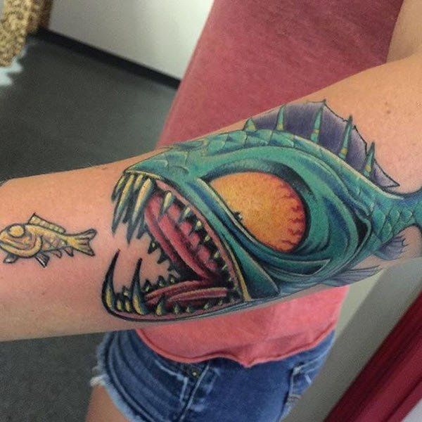Tattoo of a large, menacing turquoise fish eating a smaller fish on an arm.