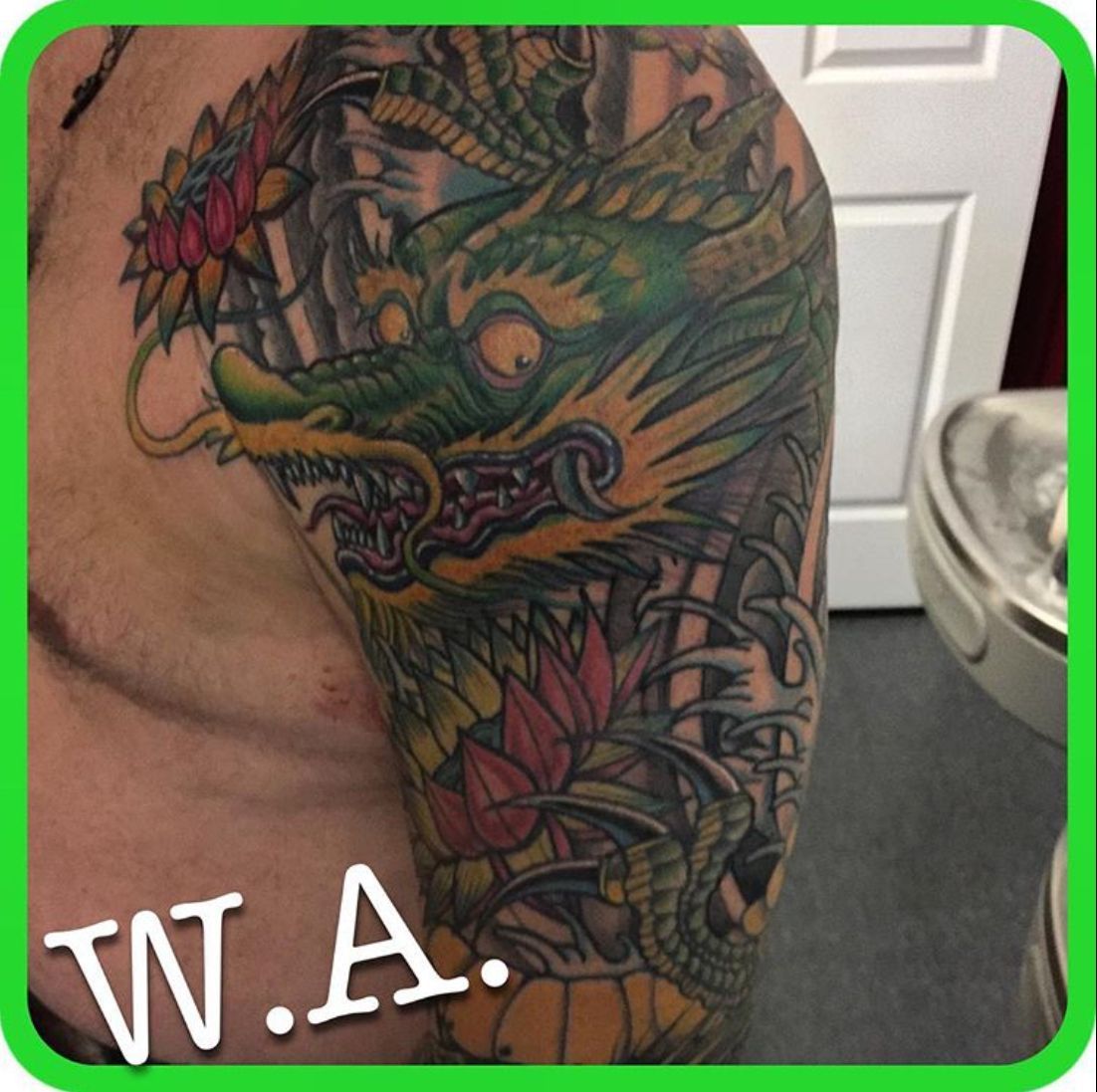 Dragon tattoo in color on a person's upper arm and shoulder. Green dragon with flowers and intricate details.