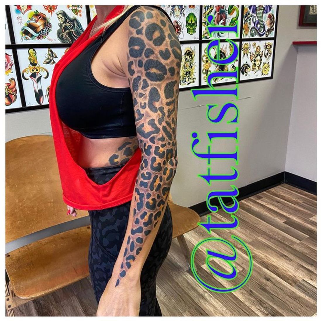 Woman with leopard-print arm tattoo, wearing a black sports bra and leggings, standing in a tattoo parlor.