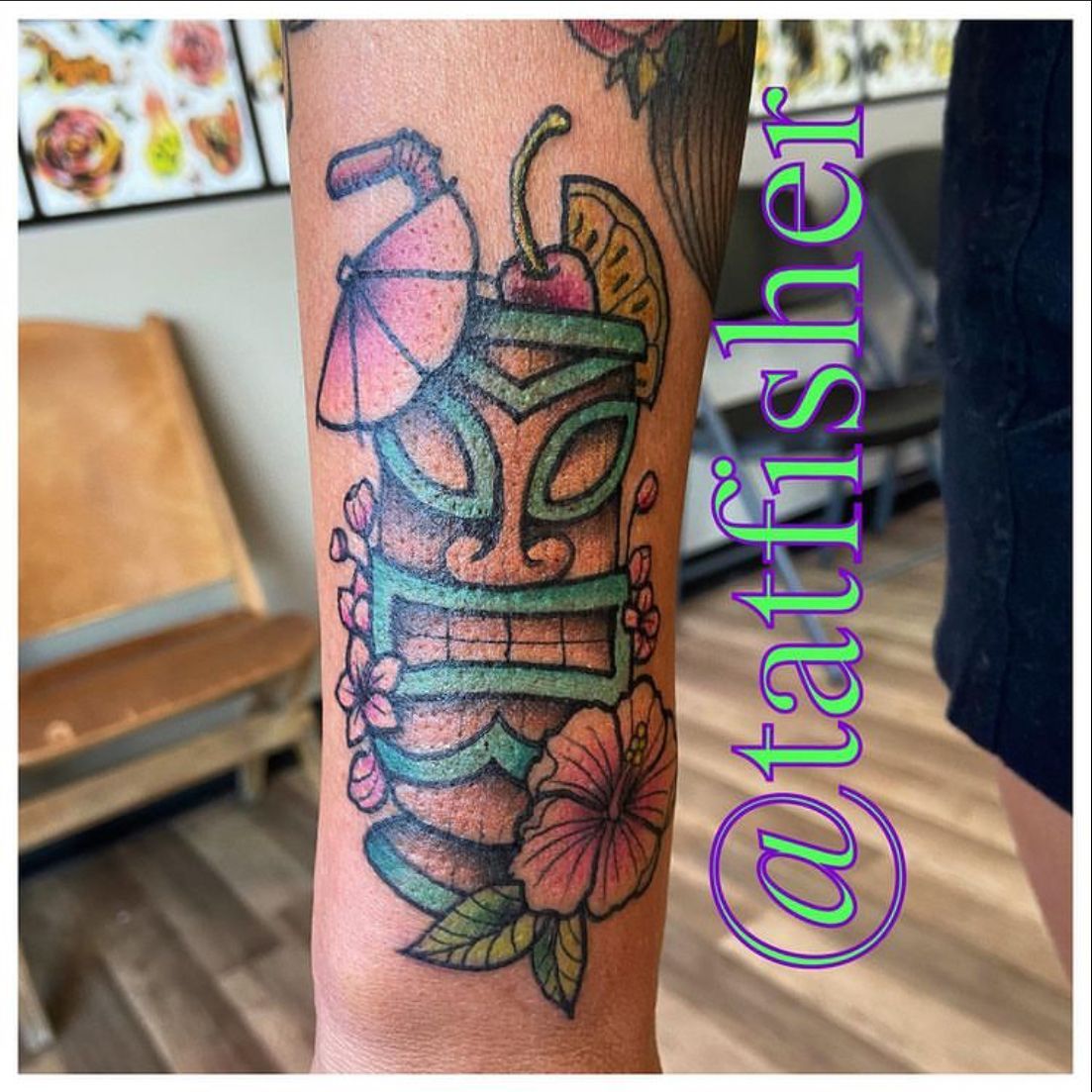 Tattoo of a colorful tiki drink with a cherry, orange slice, and flowers on a person's forearm.