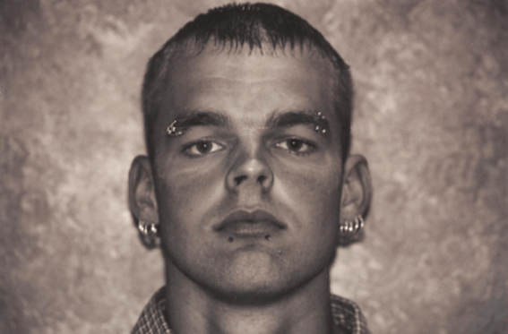 A young man with piercings in ears, eyebrows, and lip, looking directly at the viewer.