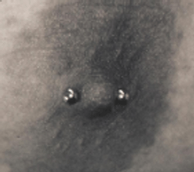 Close-up of a pierced nipple with two small, silver studs. Skin is lightly shaded.