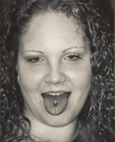 Woman with curly hair and tongue piercing, sticking out tongue.