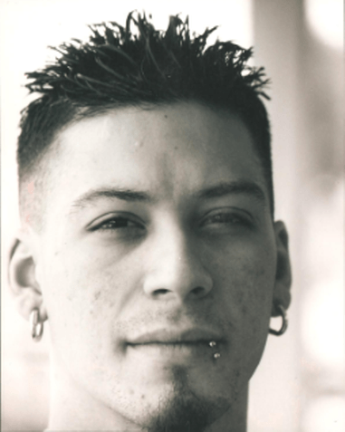 Man with spiky hair and piercings looks directly at the camera.