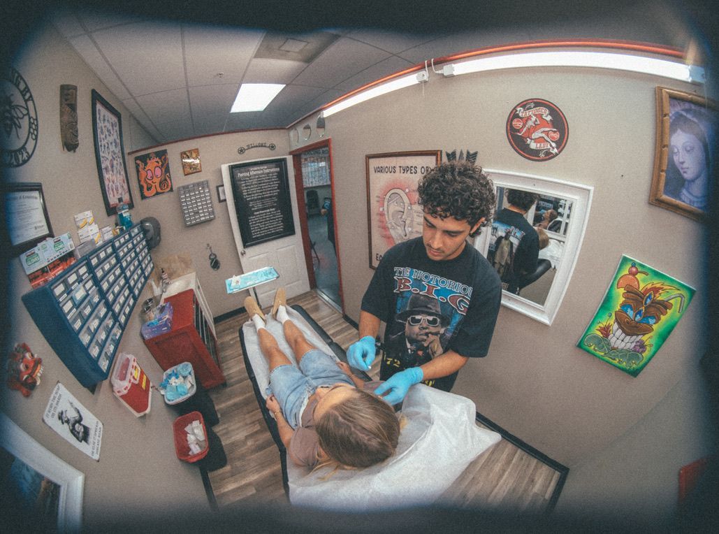 Piercing studio: artist piercing a client's neck. Artist wears gloves; client lies on a table.