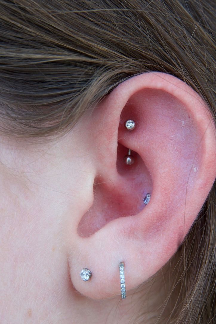 Ear with multiple piercings, including a rook, tragus, and lobe piercing with silver jewelry.