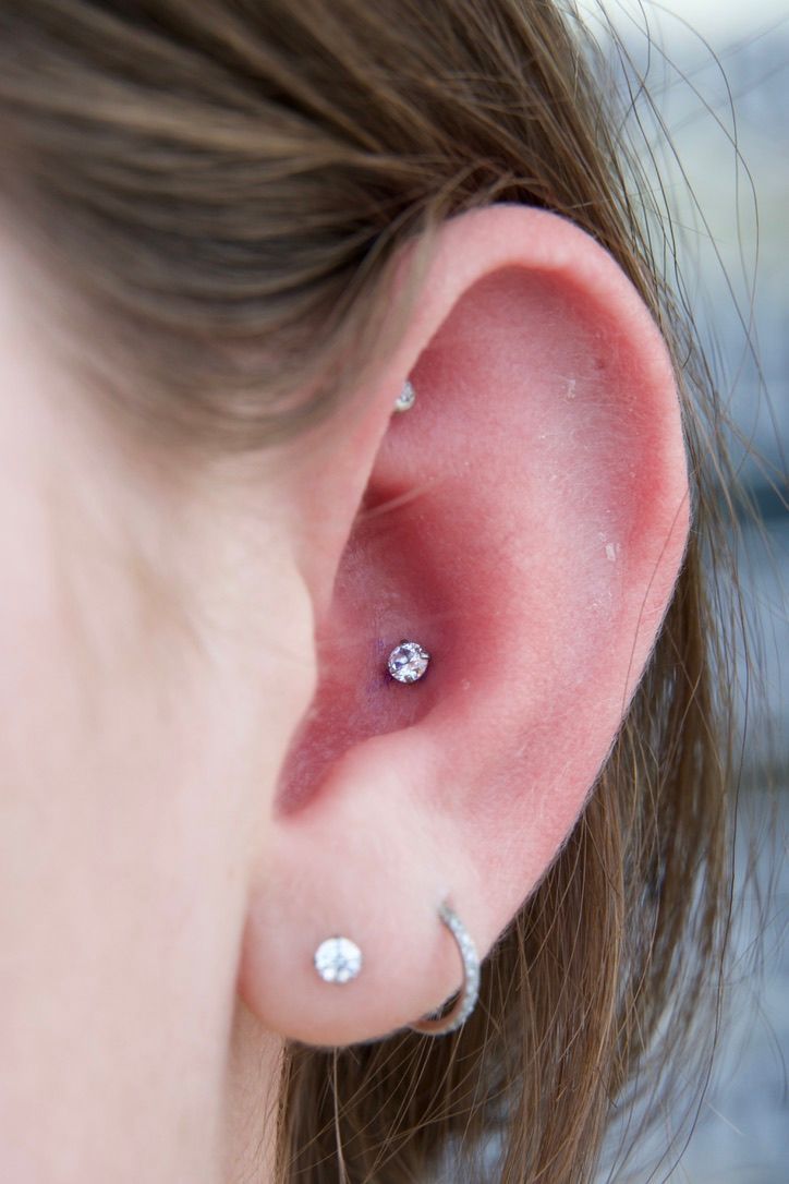 Ear with two piercings: one in the lobe with a gem, one in the inner ear with a gem, and a hoop.