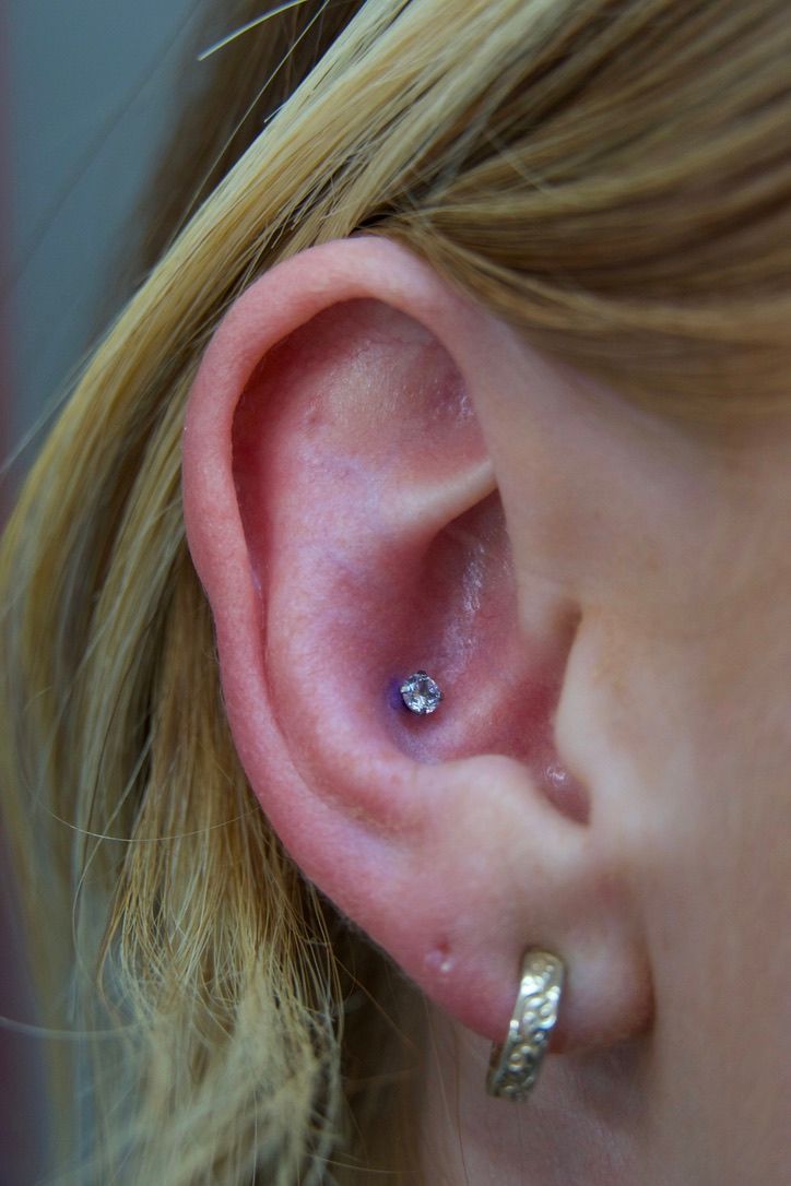 Ear with a small jeweled piercing in the conch, earring in lobe, blonde hair.