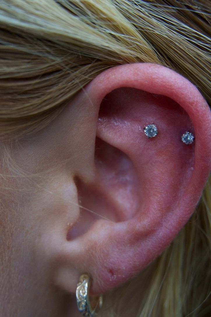 Ear with three piercings, two in the upper cartilage, and a gold hoop earring.