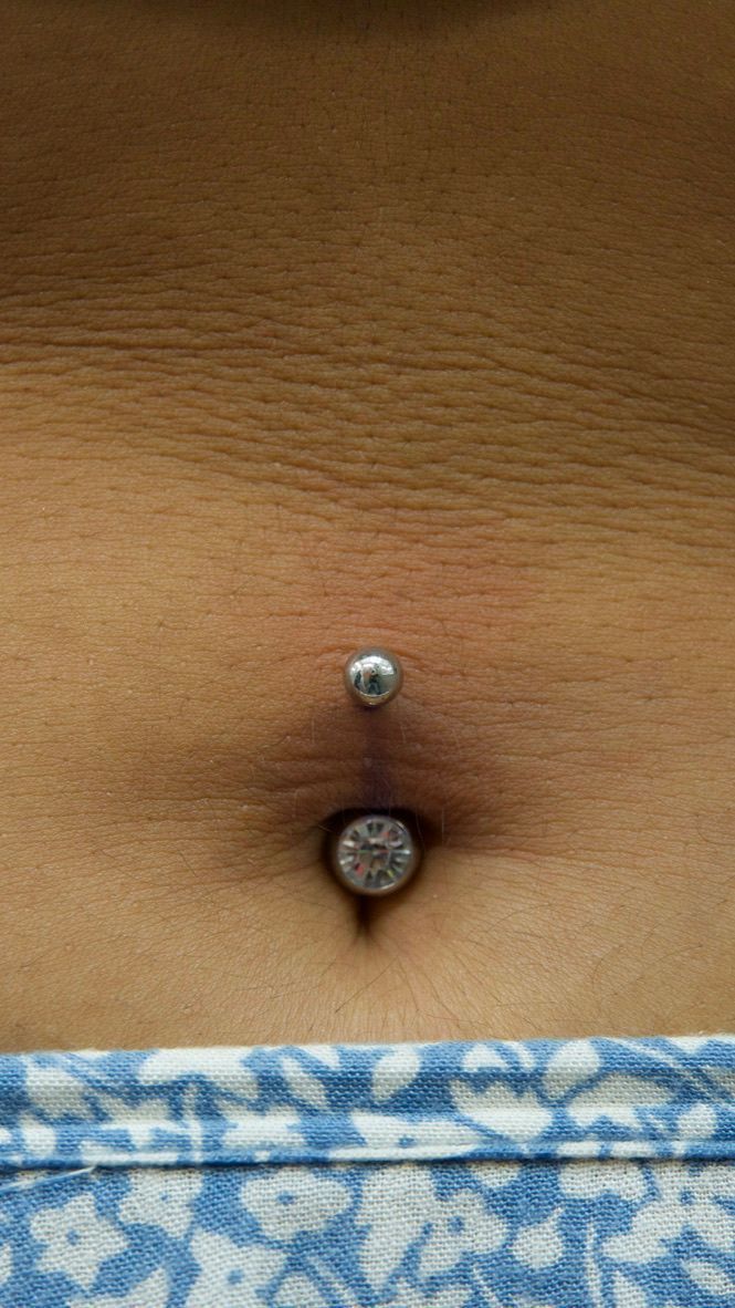 Close-up of a person's abdomen with a belly button piercing, skin is tan-colored.