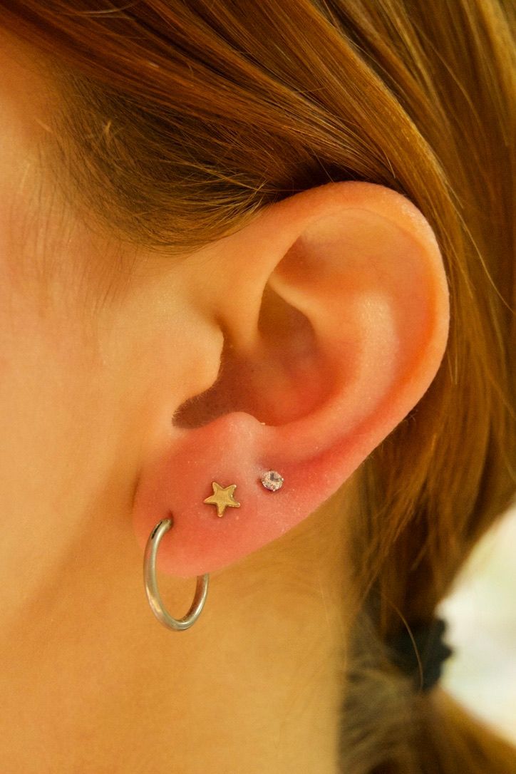 Close-up of a person's ear with three piercings: hoop, star, and small gem.