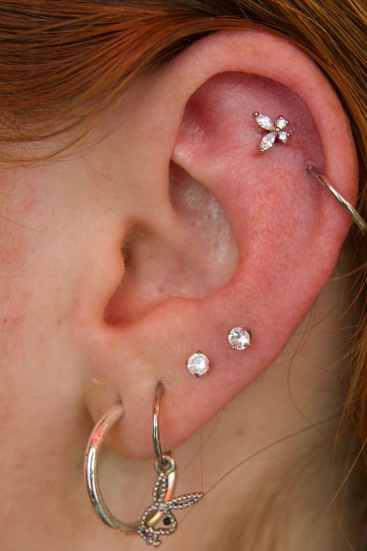 Ear with multiple piercings: helix with a floral stud, two lobe studs, and a hoop with a bunny charm.