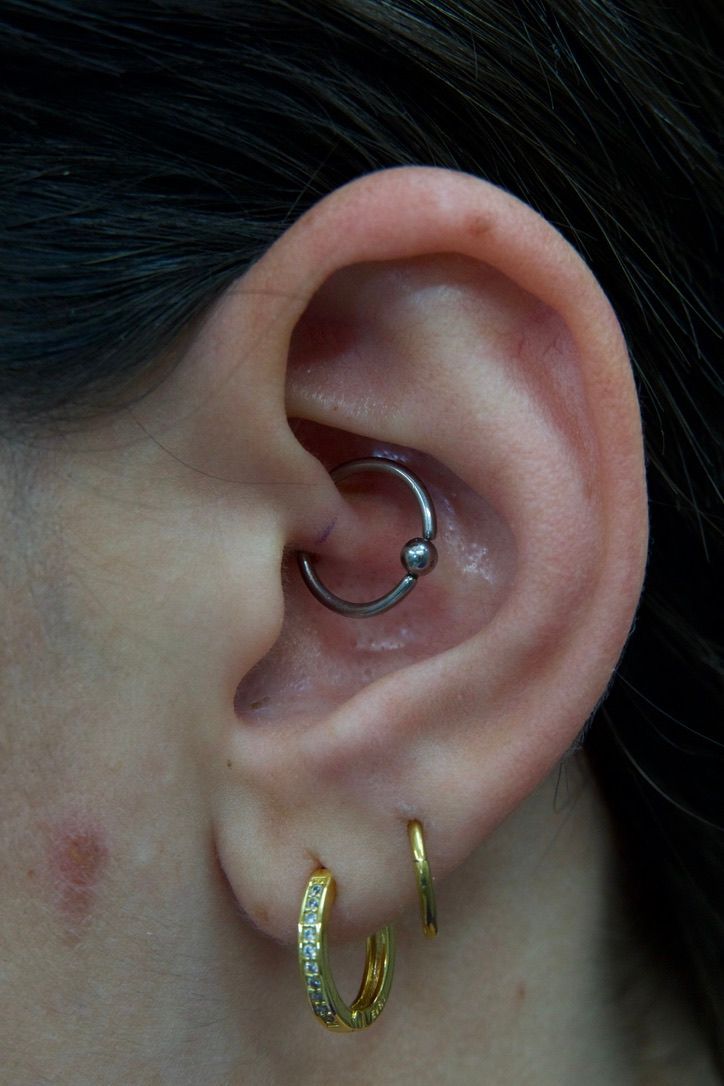 Close-up of a person's ear with a captive bead ring in the daith piercing and two gold hoop earrings.