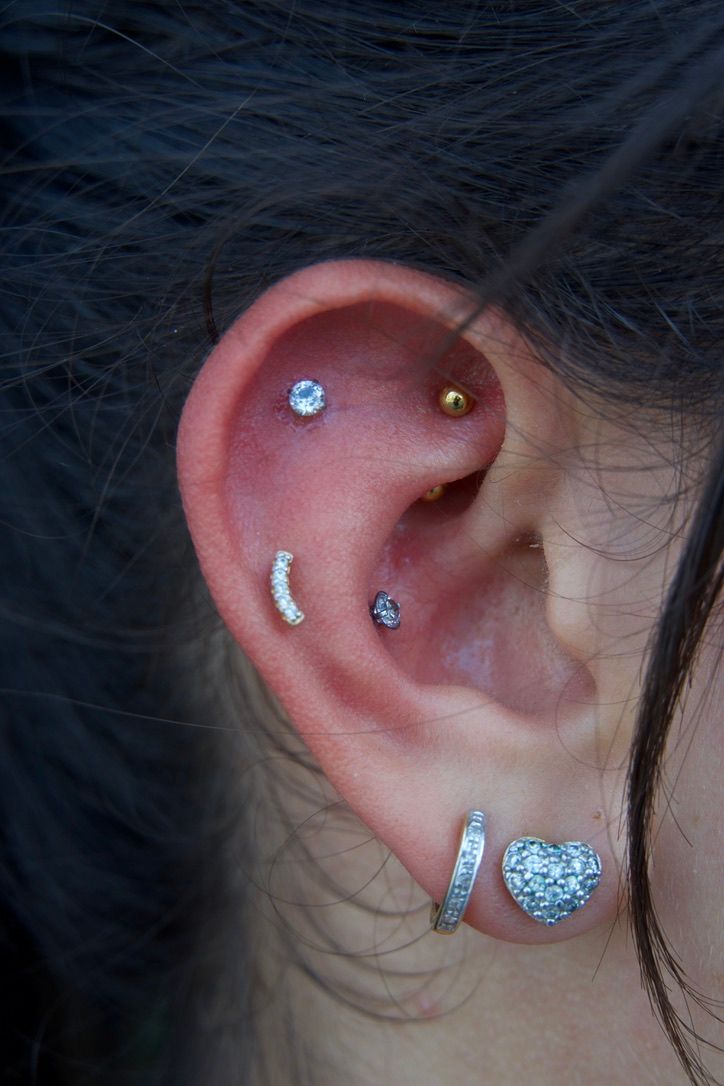 Close-up of an ear with multiple piercings and various earrings, set against dark hair and skin.