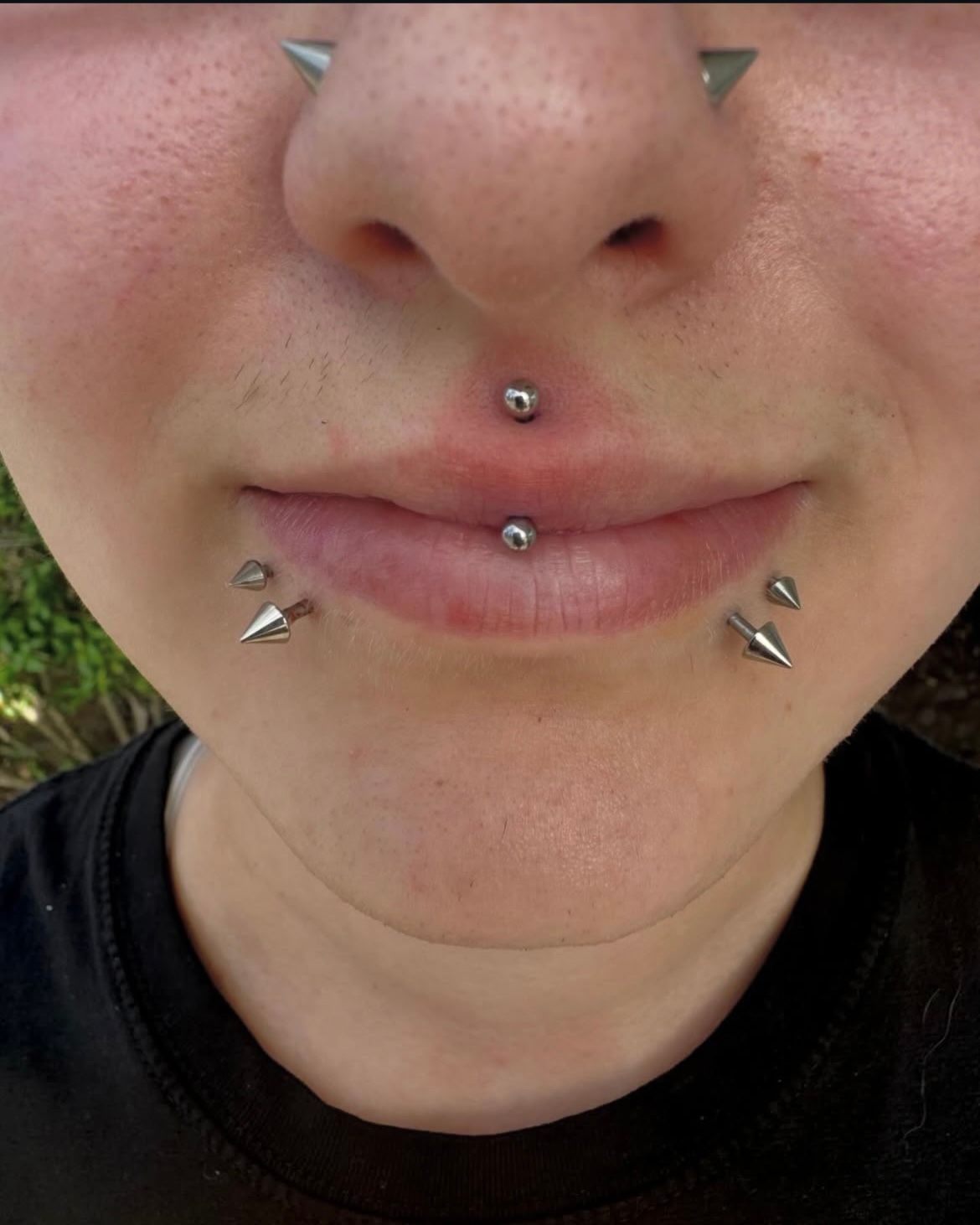 Close-up of a person's face with multiple facial piercings, including lip, nose, and cheek.